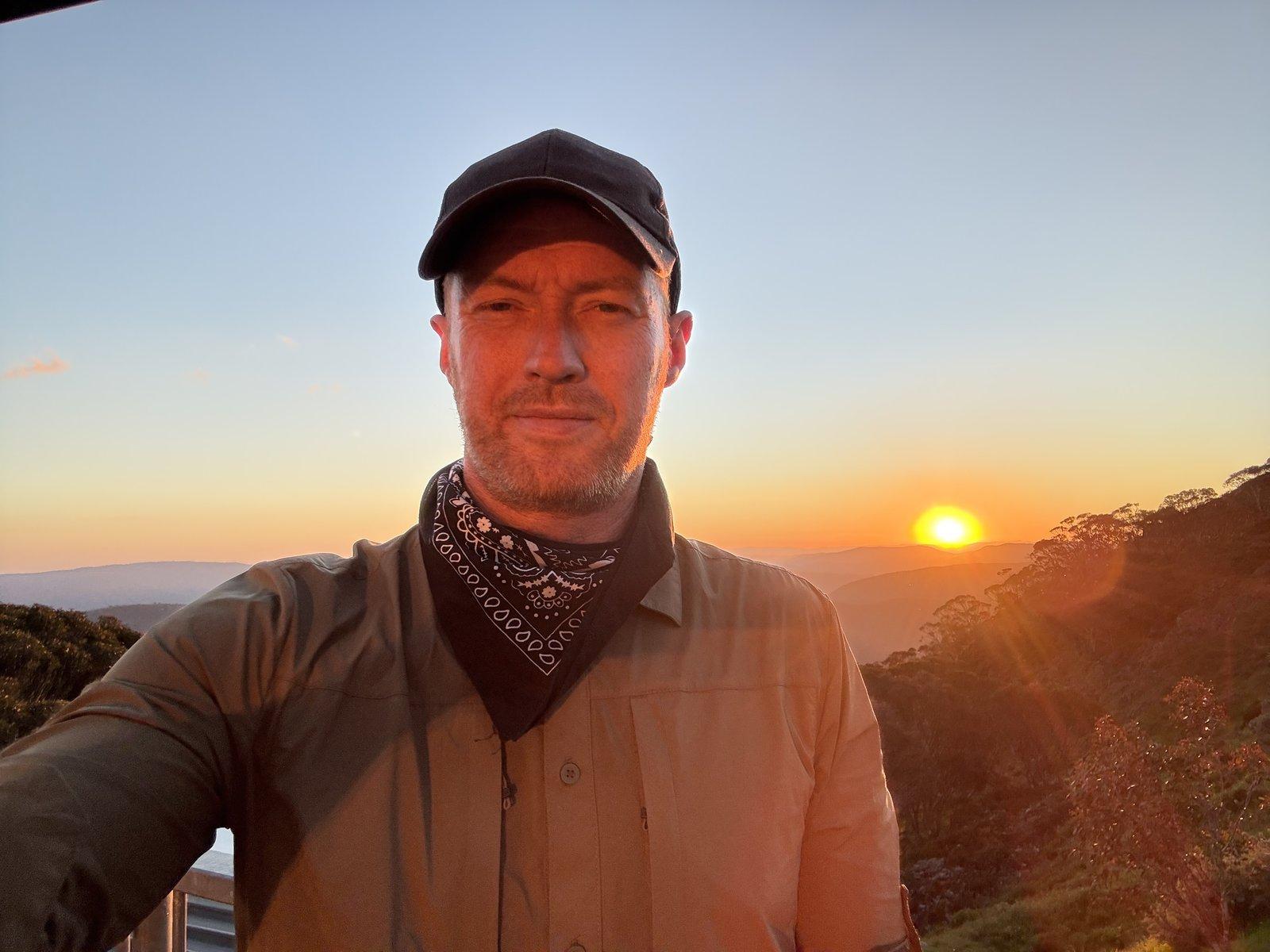 Robin at Mount Hotham at sunset — cap, bandana, the light on his face the colour of the horizon