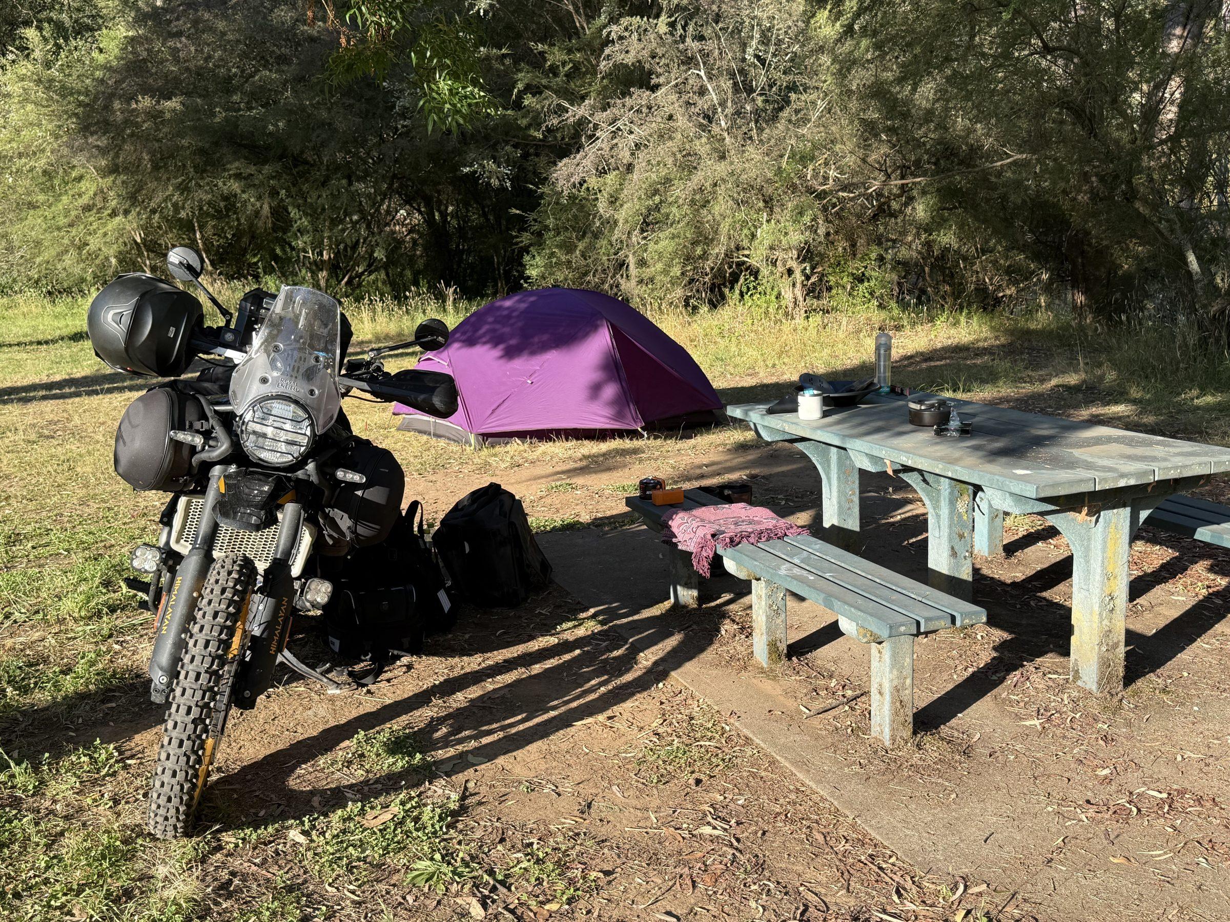 The Stacey's Bridge camp up close — Hunter with the Mitas Dakar, purple tent, picnic table, stove on the bench
