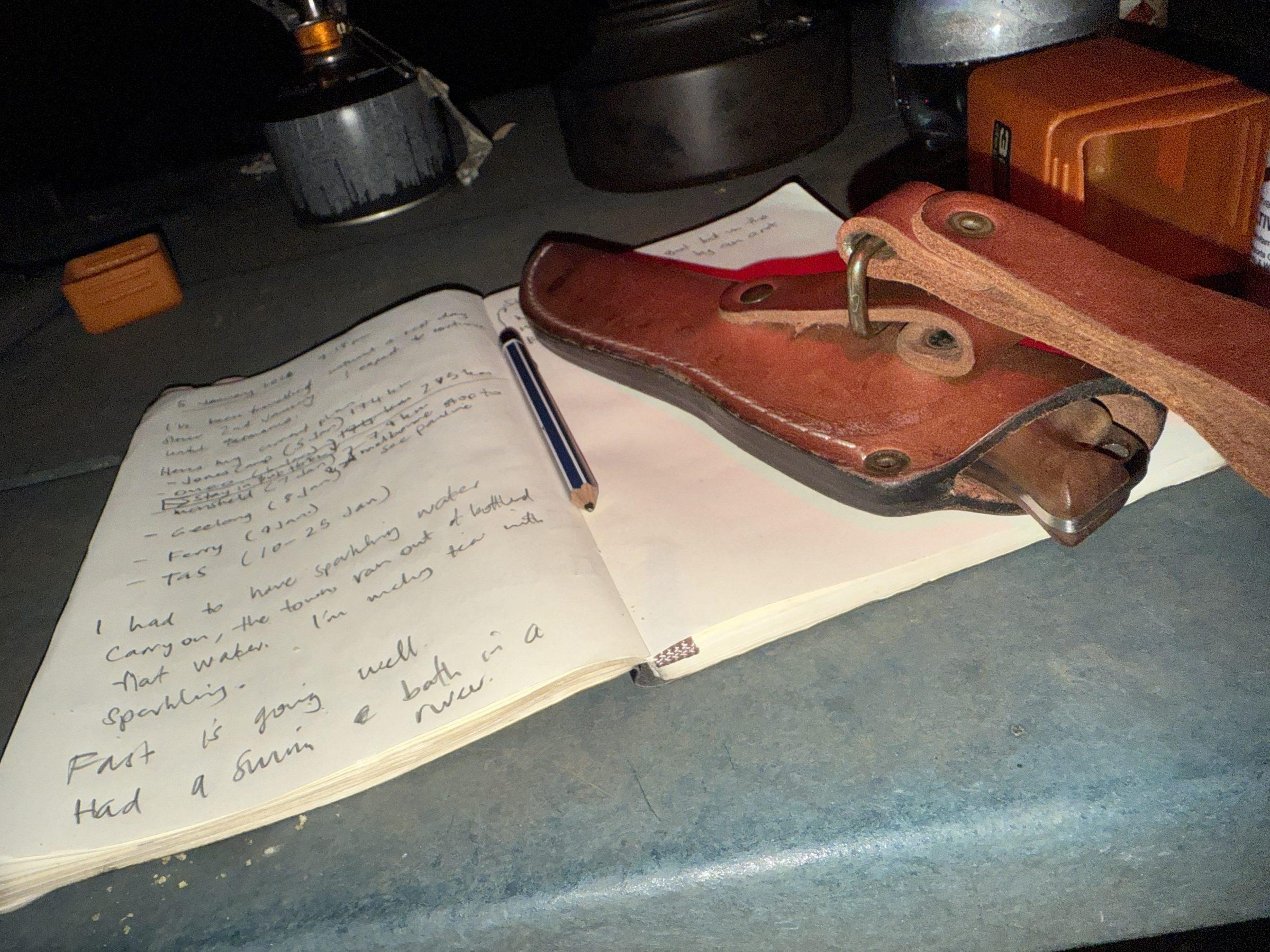 Journal open under headtorch light at camp, knife sheath beside it