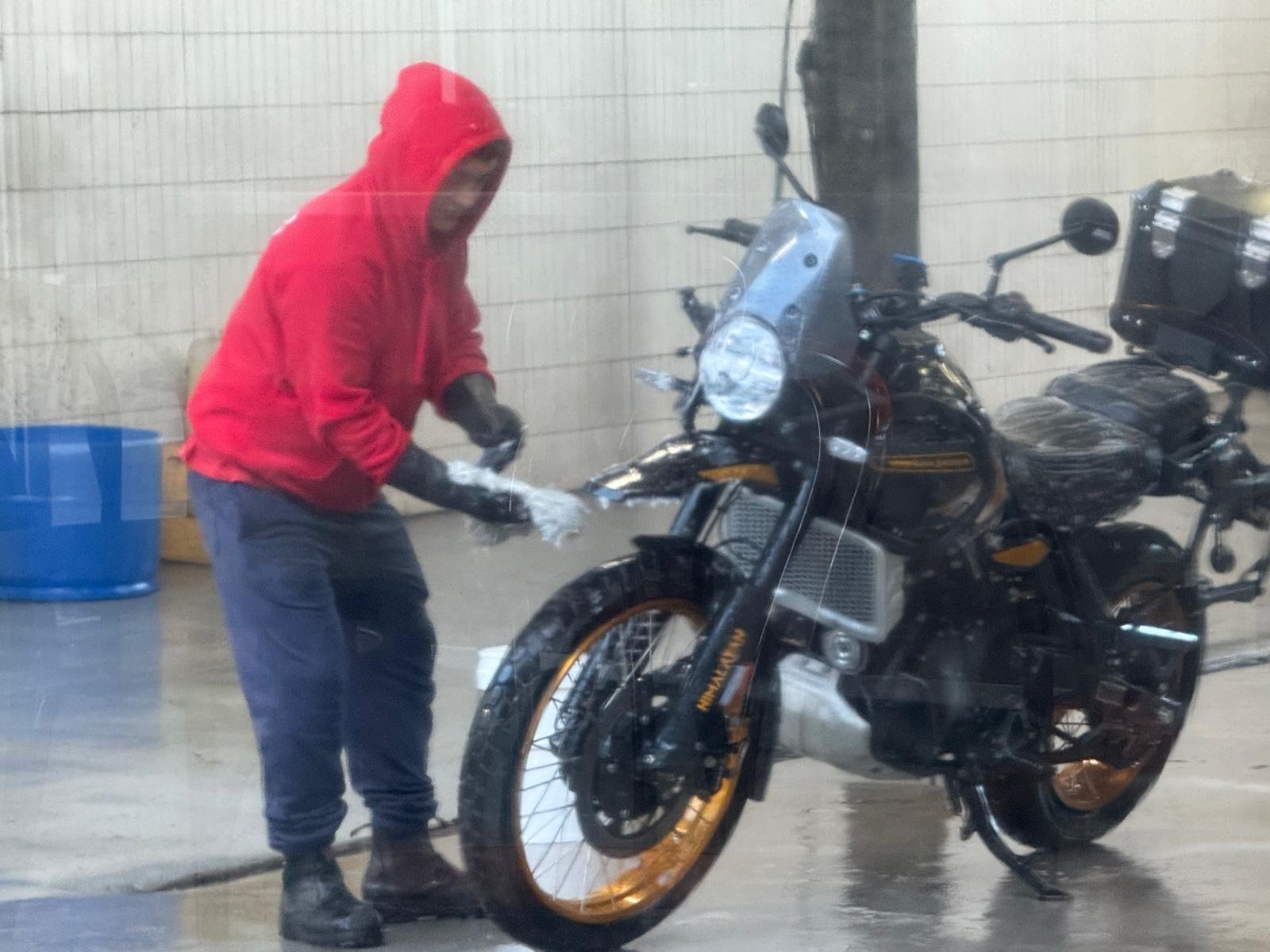 Robin in a red hoodie washing Hunter at a service-station bay after a long ride